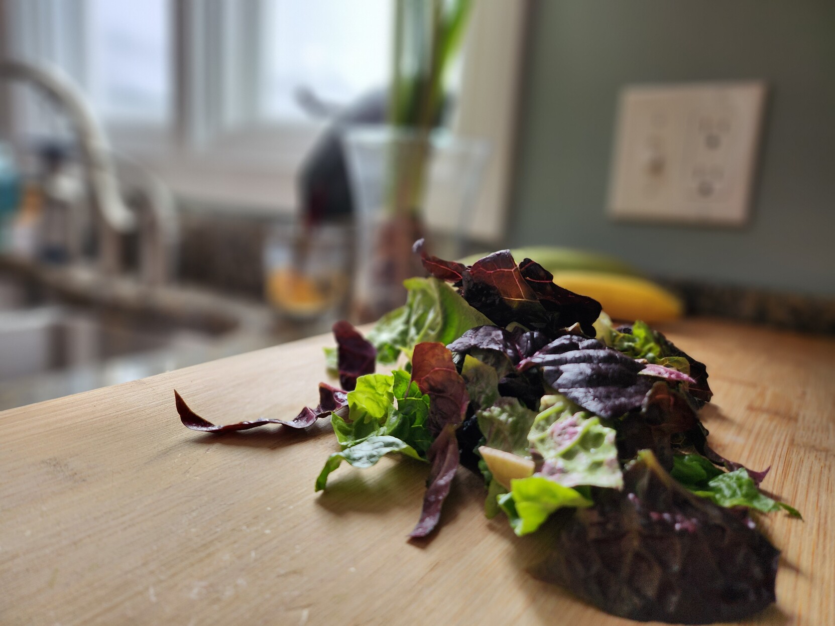 A pile of green and red leaf lettuce sits on a bamboo cutting board