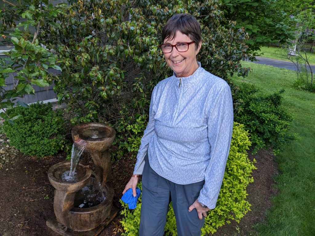 A woman standing in front of shrubs and a 3-tiered concrete fountain