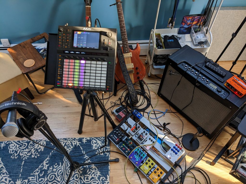 A microphone, headphones, Akai Force, pedalboard, amp, and two electric guitars are ready for action.