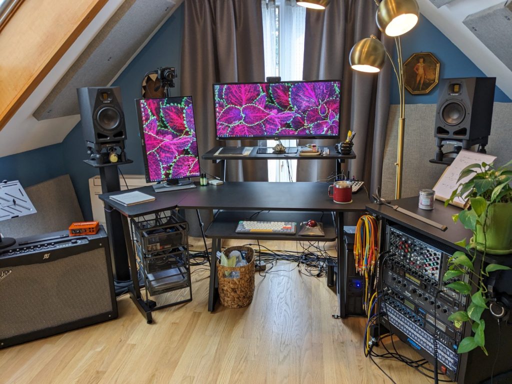 Music production computer setup with multiple monitors, outboard gear, and speakers