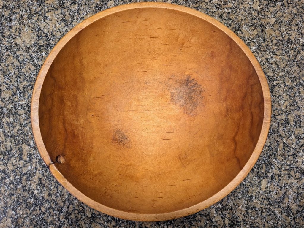 A large, handmade wooden dough-mixing bowl with a rich patina